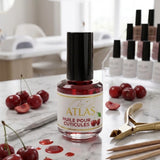 Flacon d'huile pour cuticules ATLAS parfum Cerise 15ml, accompagné de cerises fraîches sur une table de travail en marbre, utilisé en institut d'onglerie professionnel.