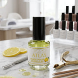 Flacon d'huile pour cuticules ATLAS parfum citron 15ml avec accessoires de manucure professionnels sur table en marbre.